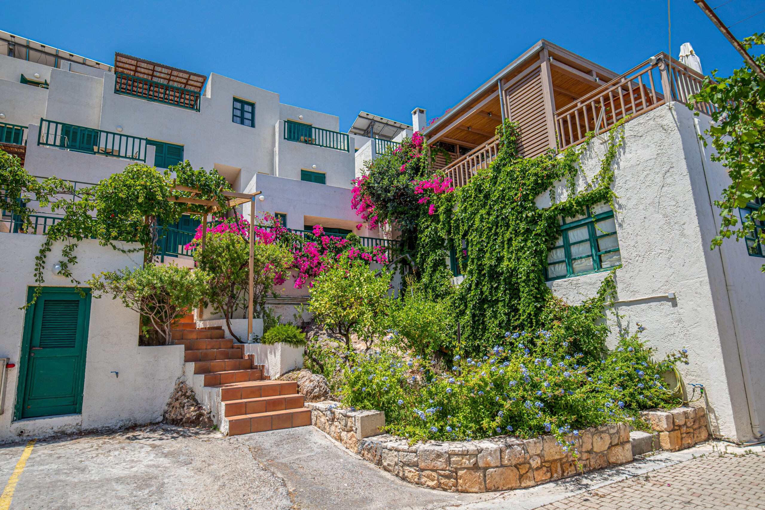 Mediterranean villa adorned with lush greenery and vibrant flowers, under a clear blue sky.