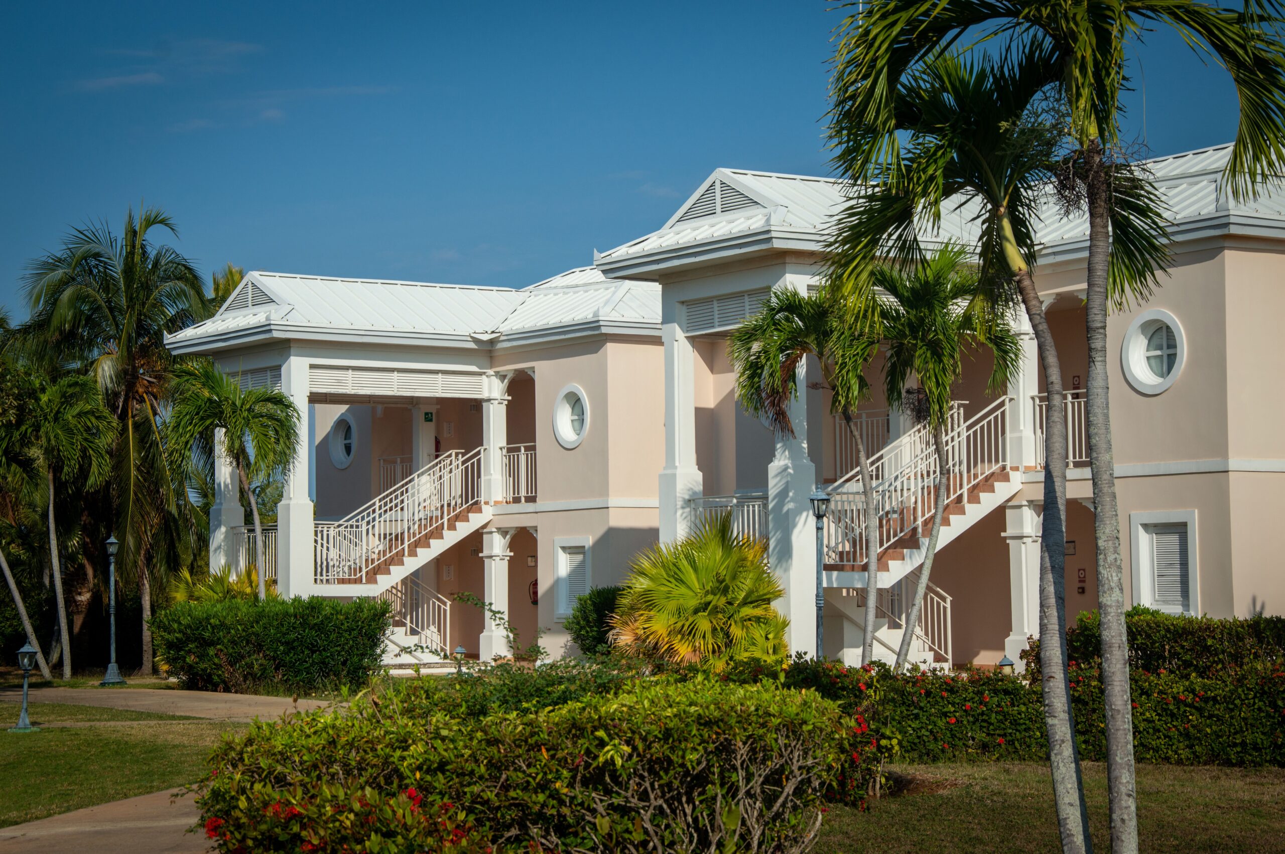 Exterior view of a tropical resort with classic architecture and lush palm trees under a clear blue sky.