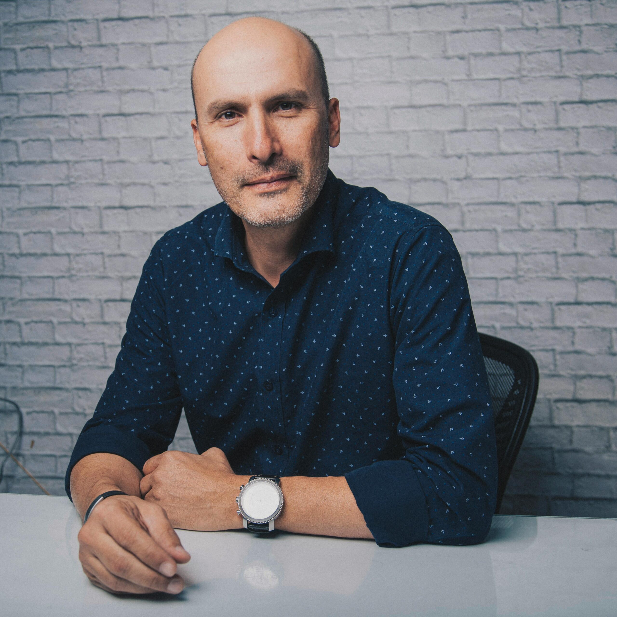 Mature confident male in shirt looking at camera while sitting on chair near white brick wall